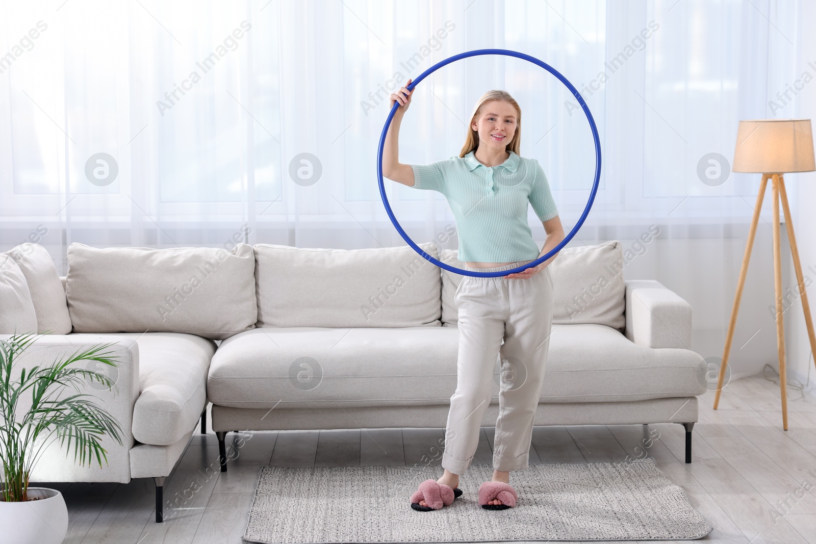 Photo of Beautiful young woman with hula hoop at home