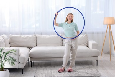 Photo of Beautiful young woman with hula hoop at home