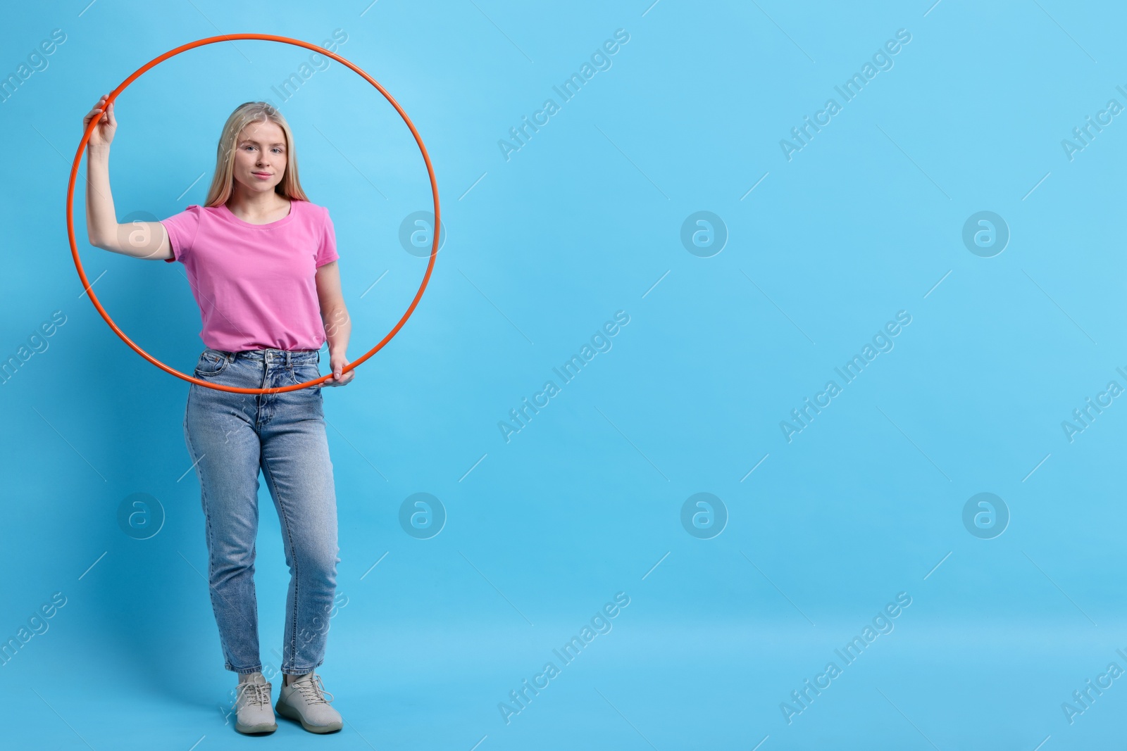 Photo of Beautiful young woman with hula hoop on light blue background, space for text