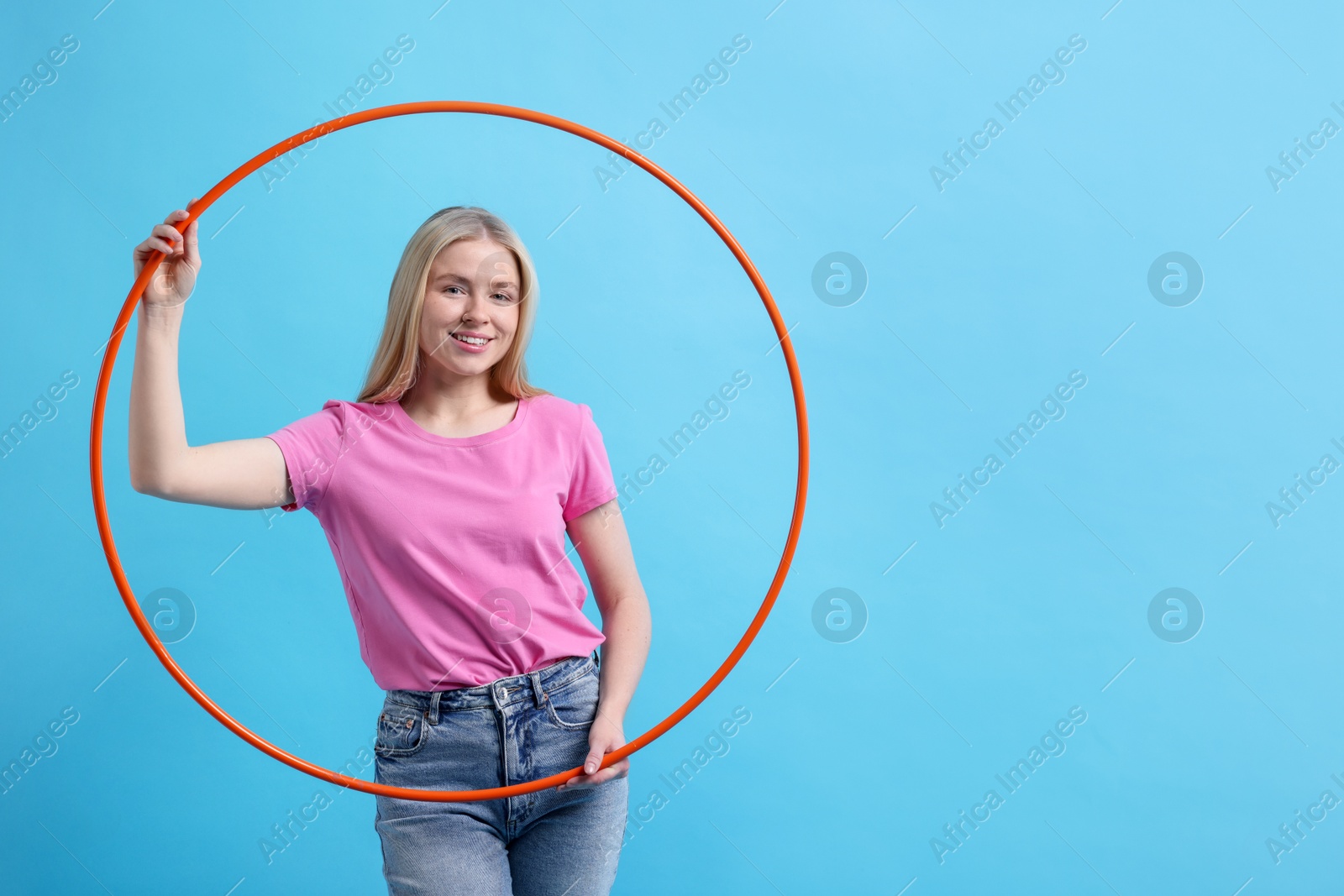 Photo of Beautiful young woman with hula hoop on light blue background, space for text