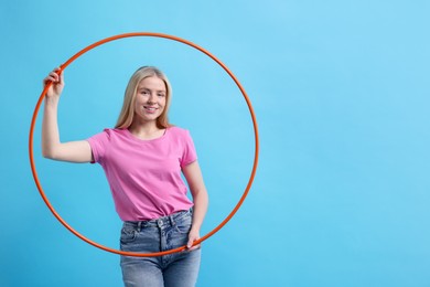 Photo of Beautiful young woman with hula hoop on light blue background, space for text