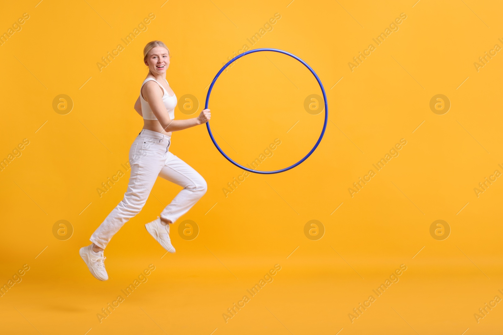 Photo of Beautiful young woman exercising with hula hoop on yellow background, space for text