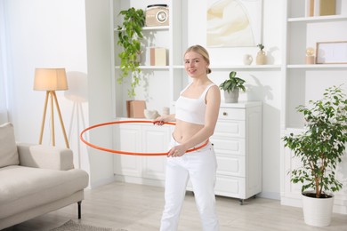 Photo of Beautiful young woman exercising with hula hoop at home