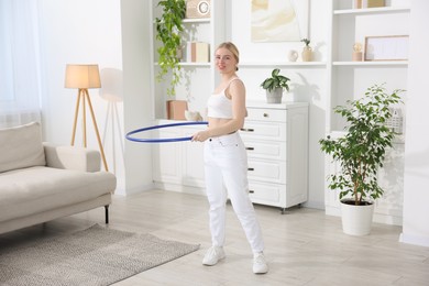 Photo of Beautiful young woman exercising with hula hoop at home