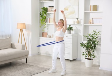 Beautiful young woman exercising with hula hoop at home