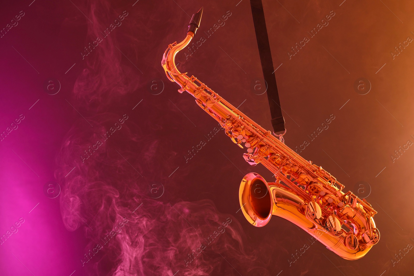 Photo of Golden saxophone on color background with smoke. Space for text