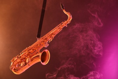 Photo of Golden saxophone on color background with smoke. Space for text