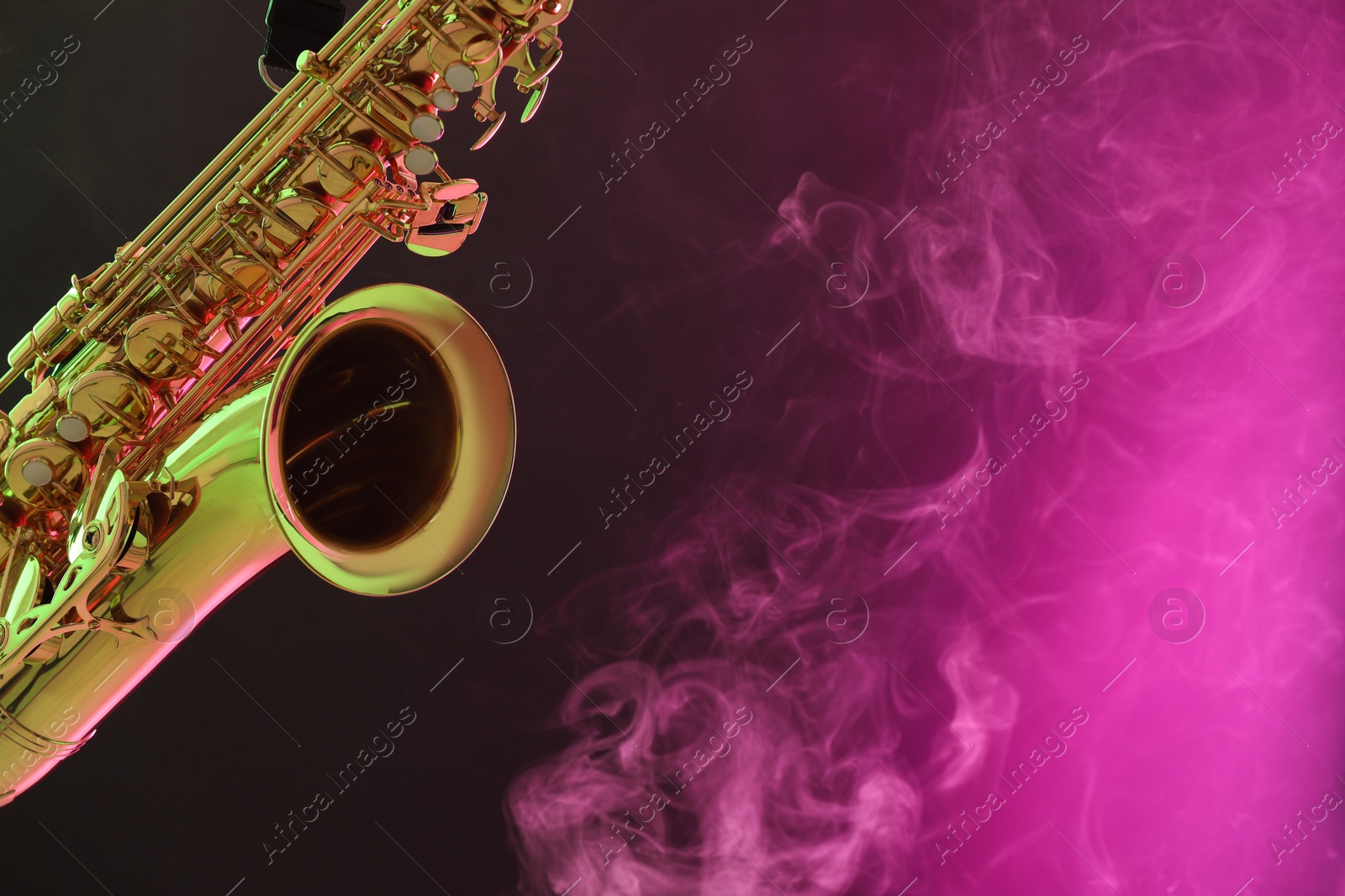 Photo of Golden saxophone on color background with smoke, closeup. Space for text