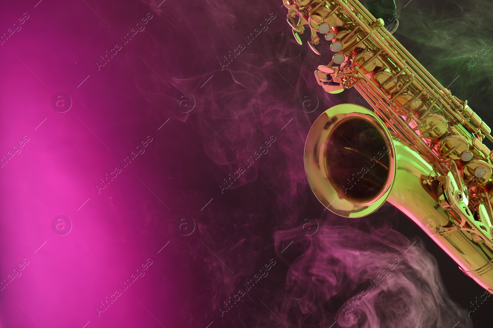 Photo of Golden saxophone on color background with smoke, closeup. Space for text