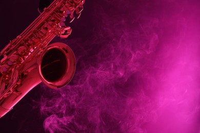 Photo of Golden saxophone on color background with smoke, closeup. Space for text