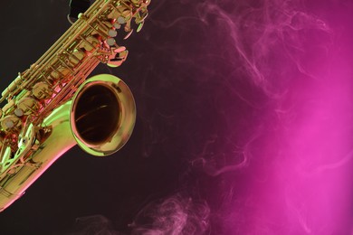 Photo of Golden saxophone on color background with smoke, closeup. Space for text