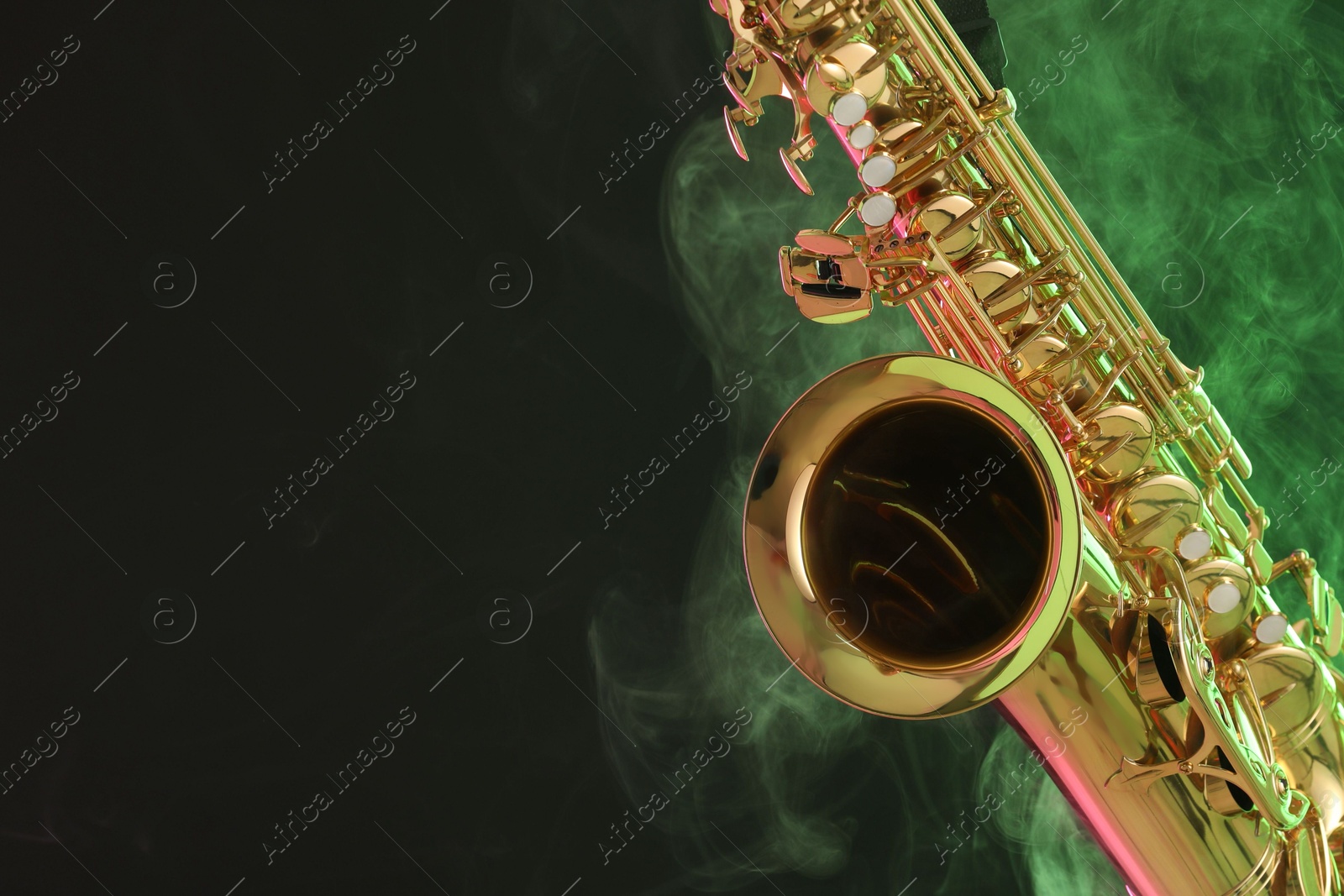 Photo of Golden saxophone on dark background with green light and smoke, closeup. Space for text