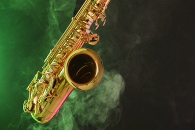 Photo of Golden saxophone on dark background with green light and smoke, closeup. Space for text