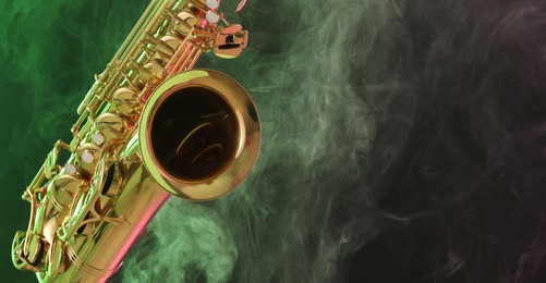 Photo of Golden saxophone on dark background with green light and smoke, closeup. Space for text