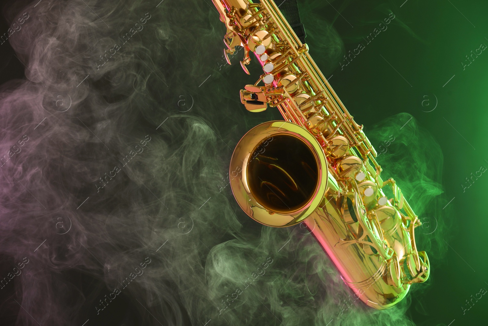 Photo of Golden saxophone on dark background with green light and smoke, closeup. Space for text