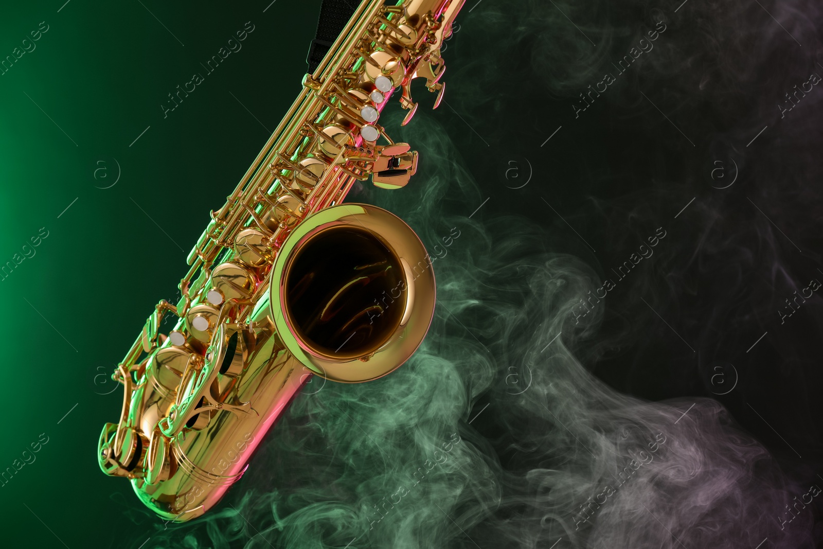 Photo of Golden saxophone on dark background with green light and smoke, closeup. Space for text