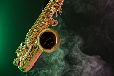 Photo of Golden saxophone on dark background with green light and smoke, closeup. Space for text