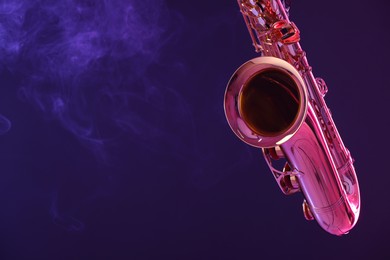 Photo of Golden saxophone on dark background with neon lights and smoke, closeup. Space for text