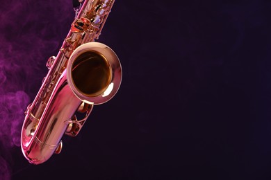 Photo of Golden saxophone on dark background with neon lights and smoke, closeup. Space for text