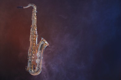 Photo of Golden saxophone on dark background with smoke. Space for text