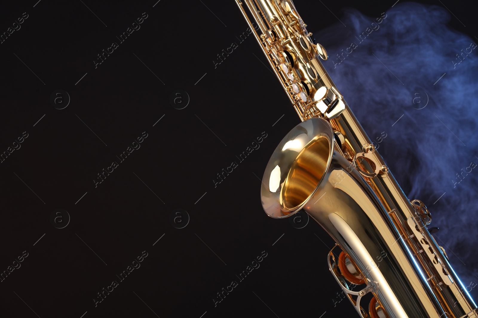 Photo of Golden saxophone on black background with smoke, closeup. Space for text