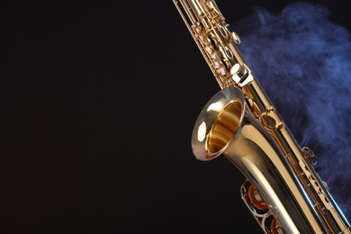 Photo of Golden saxophone on black background with smoke, closeup. Space for text