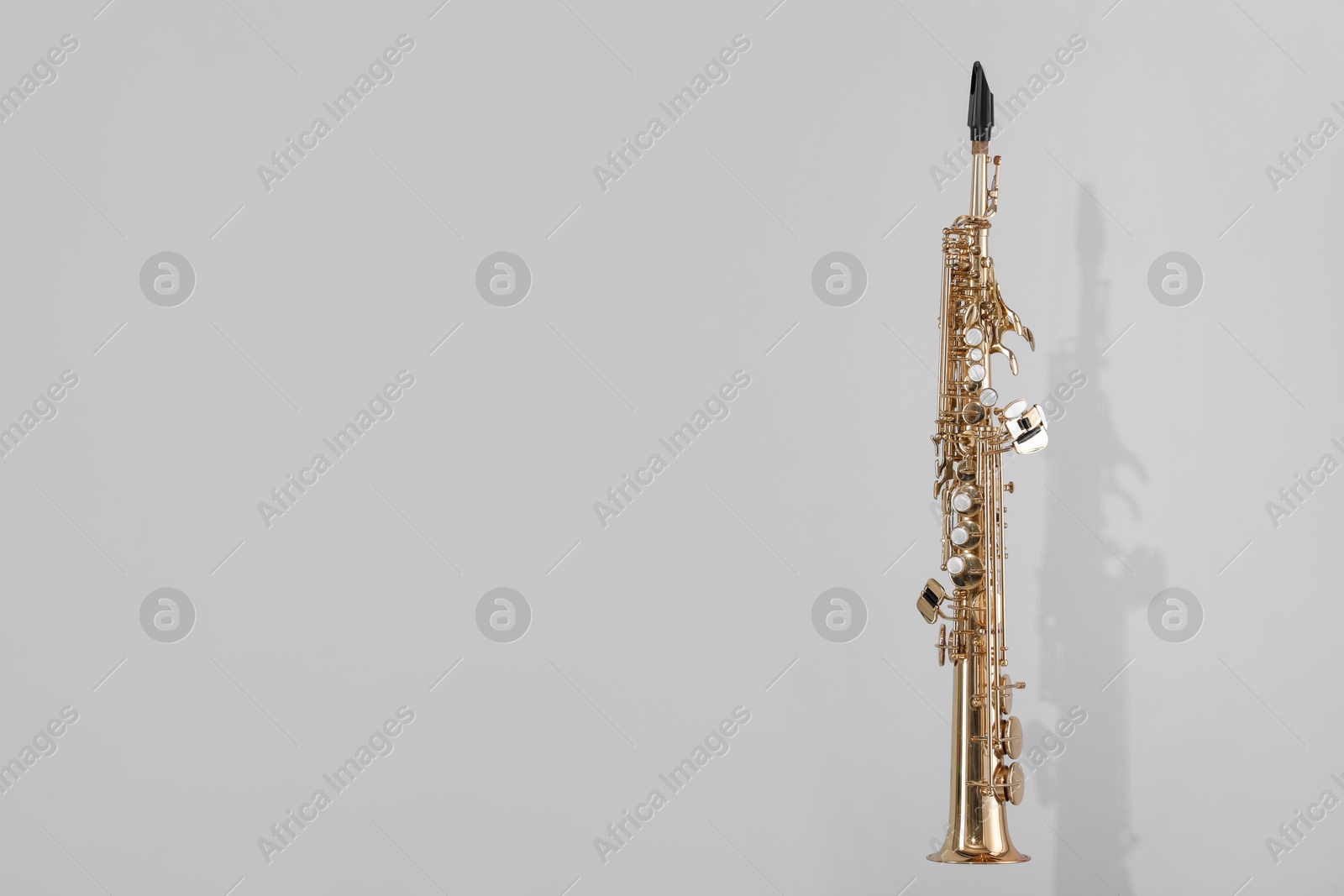 Photo of Golden soprano saxophone on light grey background. Space for text