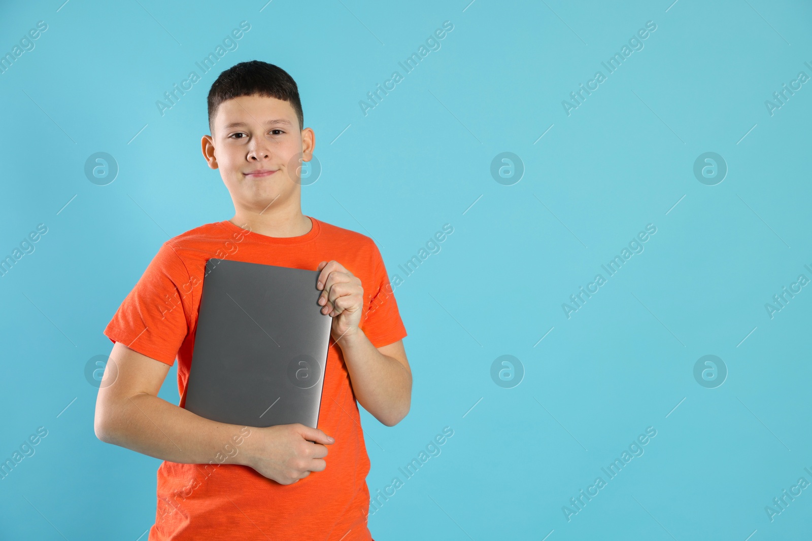 Photo of Portrait of teenage boy with laptop on light blue background, space for text