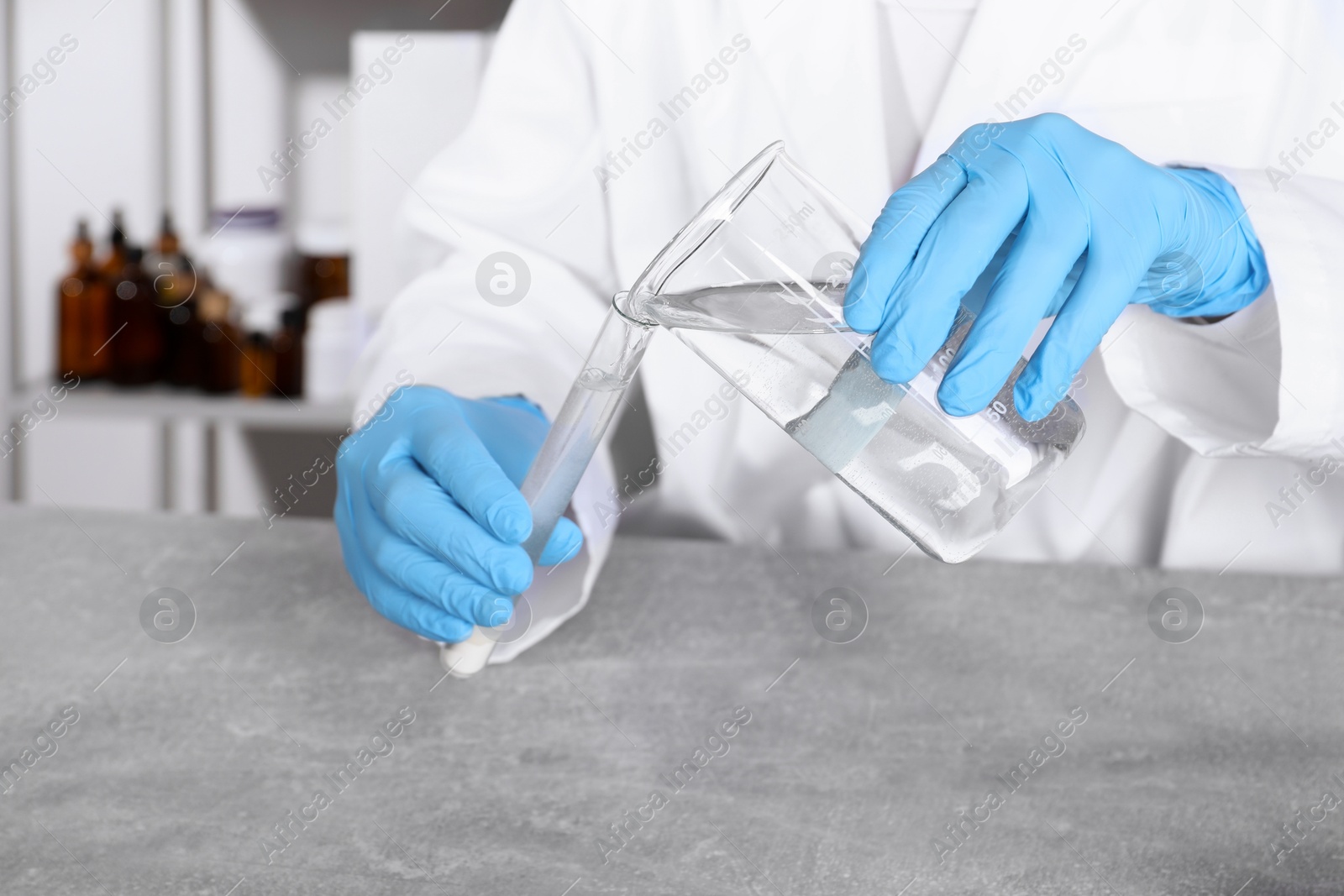 Photo of Laboratory testing. Scientist pouring liquid into test tube at grey table indoors, closeup