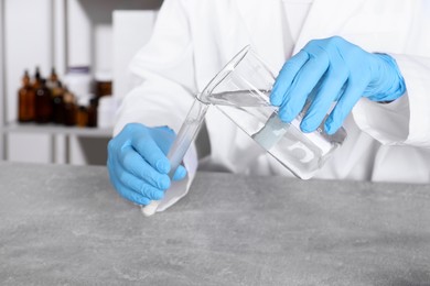 Photo of Laboratory testing. Scientist pouring liquid into test tube at grey table indoors, closeup