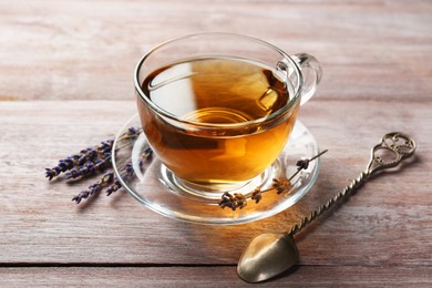 Photo of Aromatic lavender tea in glass cup, spoon and dry flowers on wooden table, closeup