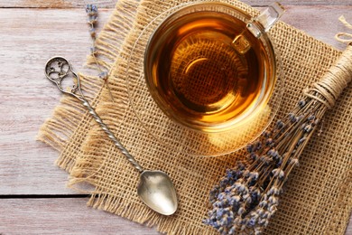 Photo of Aromatic lavender tea in glass cup, spoon and dry flowers on wooden table, flat lay