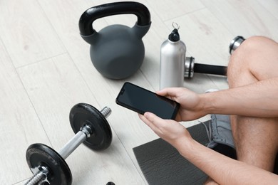 Photo of Man with smartphone and gym equipment on floor indoors, above view