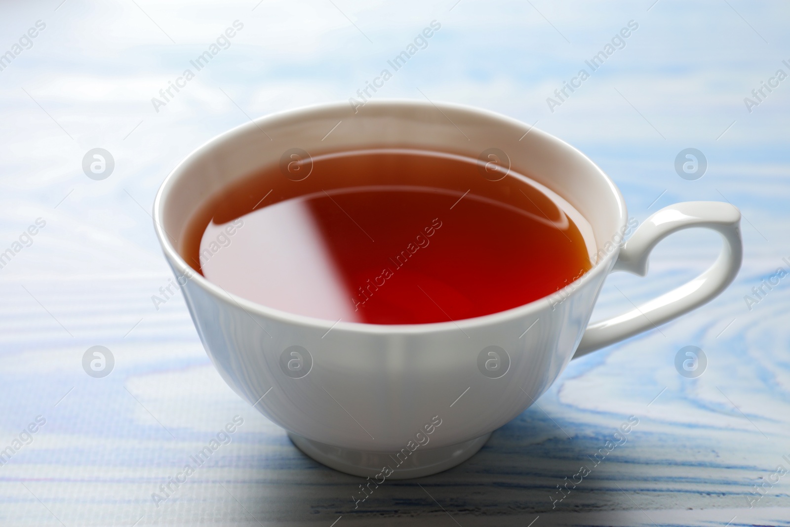 Photo of Aromatic black tea in cup on light blue wooden table, closeup