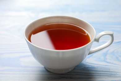 Aromatic black tea in cup on light blue wooden table, closeup