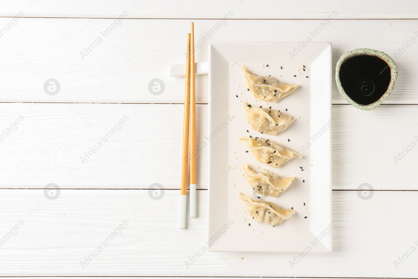 Photo of Delicious gyoza dumplings with sesame seeds served on white wooden table, top view. Space for text