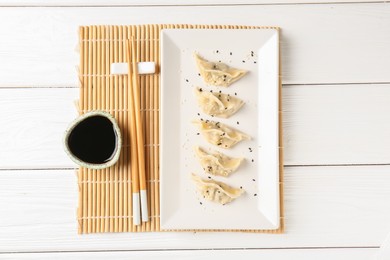 Photo of Delicious gyoza dumplings with sesame seeds served on white wooden table, top view