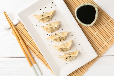 Photo of Delicious gyoza dumplings with sesame seeds served on white wooden table, top view