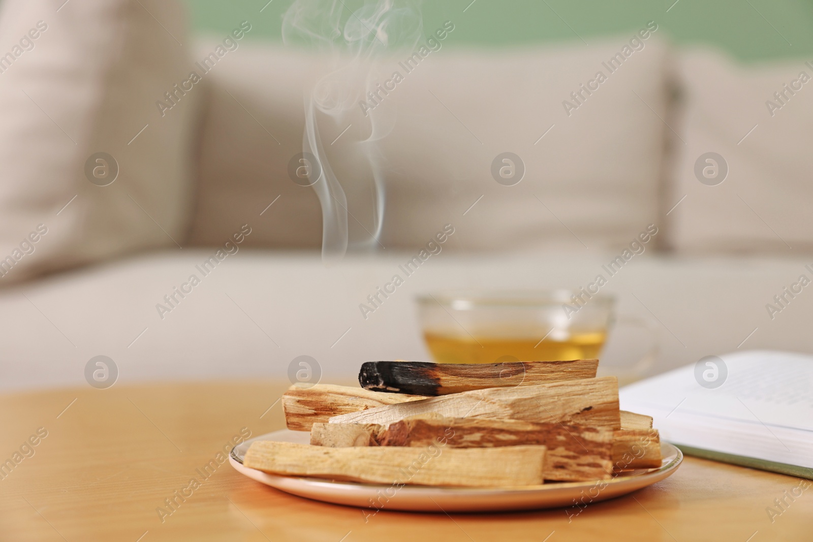 Photo of Palo santo sticks and smoldering one on wooden table indoors, space for text