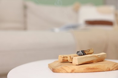 Photo of Palo santo sticks and burnt one on white table indoors, space for text