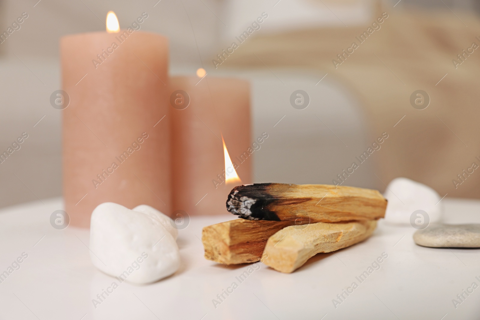 Photo of Palo santo sticks, burning candles and stones on white table indoors, closeup