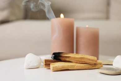 Photo of Palo santo sticks, burning candles and stones on white table indoors, space for text