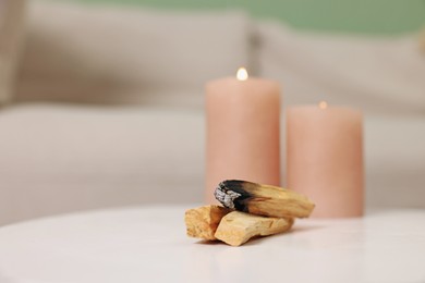 Photo of Palo santo sticks and burning candles on white table indoors, space for text