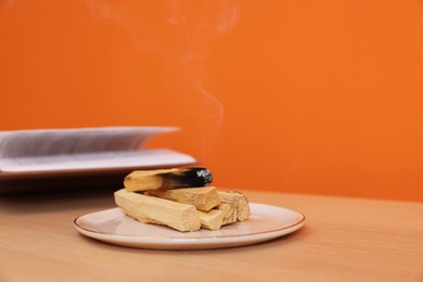 Photo of Palo santo sticks and smoldering one wooden table against orange wall, space for text