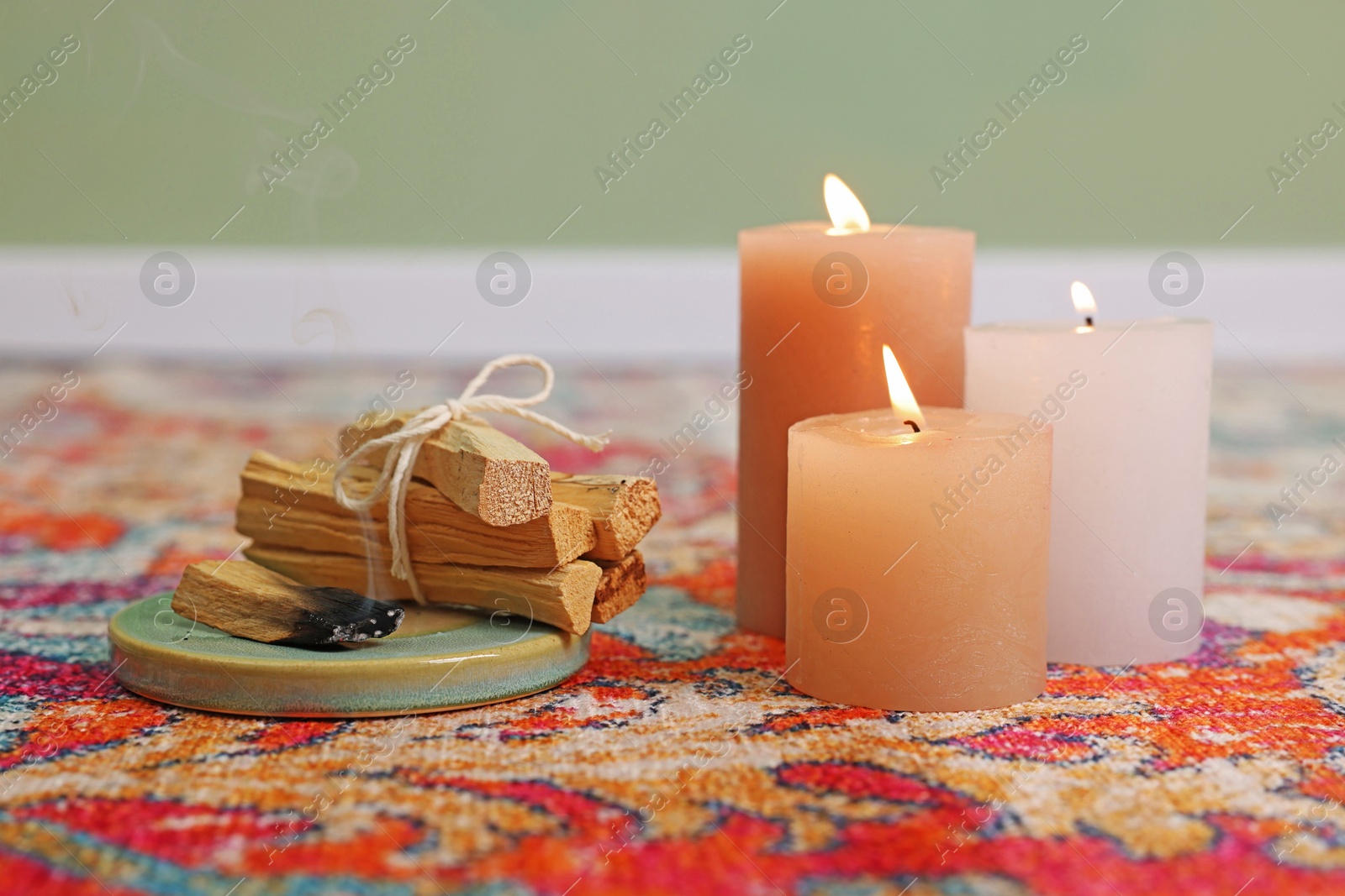 Photo of Palo santo sticks and burning candles on rug indoors