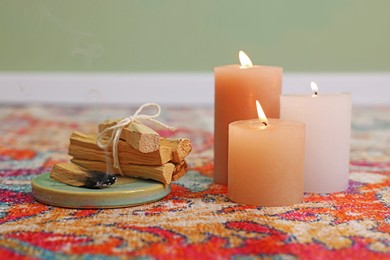 Photo of Palo santo sticks and burning candles on rug indoors