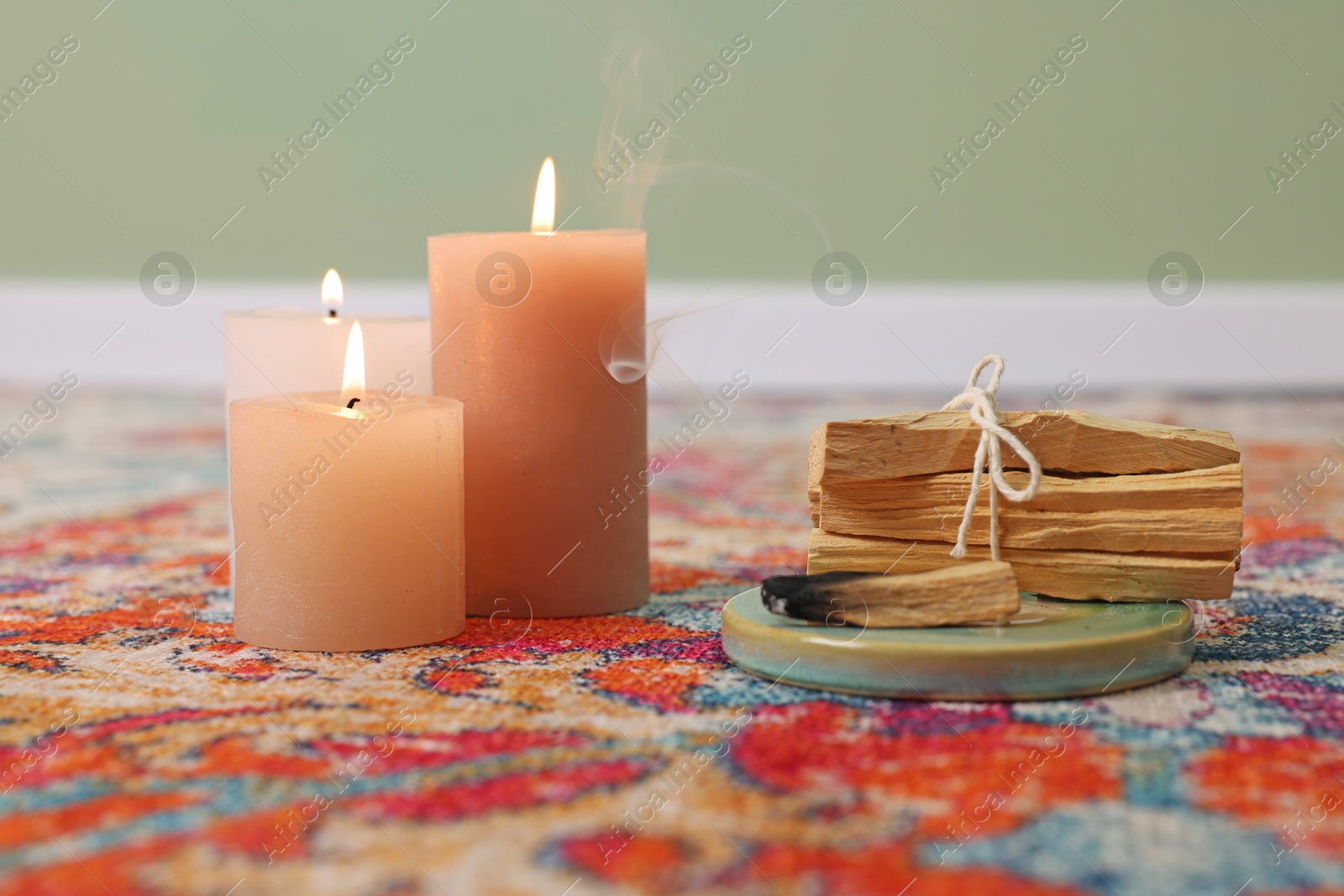 Photo of Palo santo sticks and burning candles on rug indoors