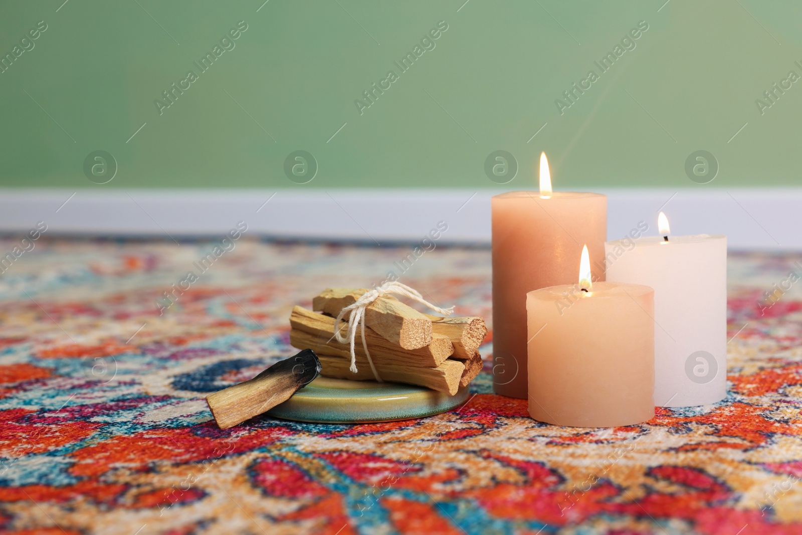 Photo of Palo santo sticks and burning candles on rug indoors, space for text