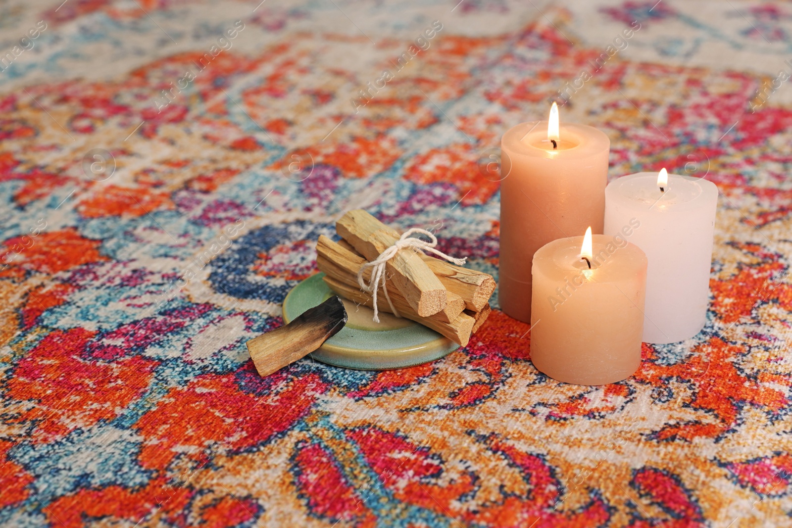 Photo of Palo santo sticks and burning candles on rug indoors, space for text