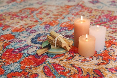 Photo of Palo santo sticks and burning candles on rug indoors, space for text